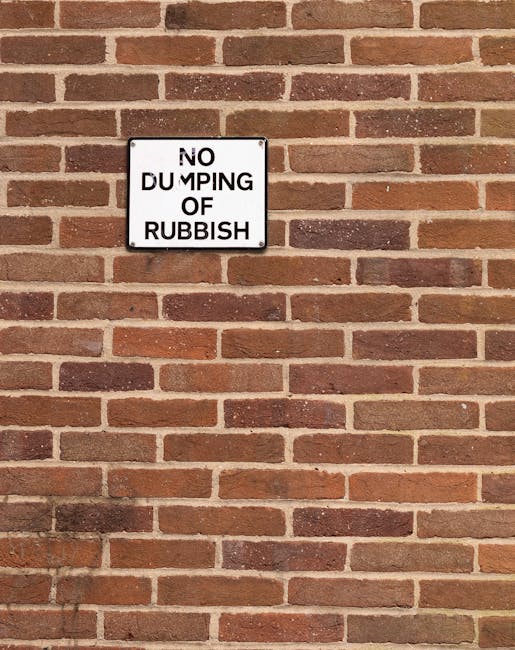 In an urban outdoor setting, a large, rectangular, metal skip with a weathered red finish is positioned against a grey concrete wall, partially recessed into a corner formed by a dark, textured wall o